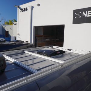 New Way Van Life silver aluminum roof rack installed on a 2021 Mercedes Sprinter van with a MaxxAir MaxxFan vent mounted on the platform, photographed outside the New Way Van Life facility in San Diego