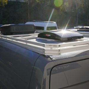 New Way Van Life silver aluminum roof rack installed on a 2022-2026 Mercedes Sprinter van with a MaxxAir MaxxFan roof vent and rooftop AC unit mounted on the platform shown from a rear three-quarter angle