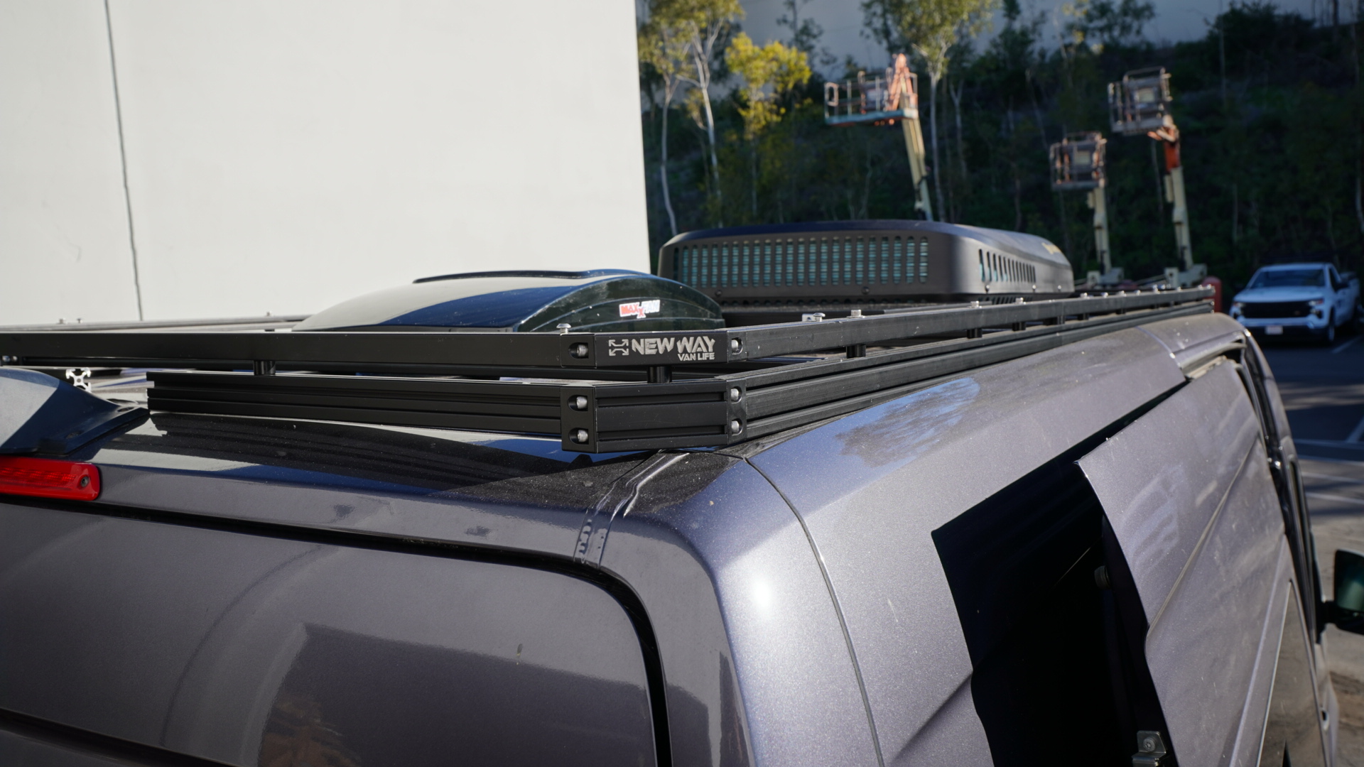 New Way Van Life aluminum roof rack installed on a 2022 Mercedes Sprinter van shown from the rear corner angle with MaxxFan vent and rooftop AC unit mounted on the platform
