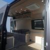 75" 3-door birch overhead cabinet installed in a Mercedes Sprinter van conversion with lift-assisted doors open, showing interior storage and integrated underlighting