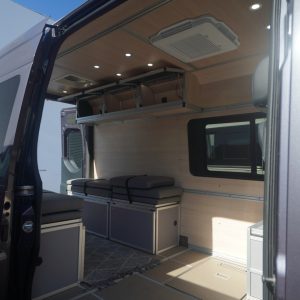 75" 3-door birch overhead cabinet installed in a Mercedes Sprinter van conversion with lift-assisted doors open, showing interior storage and integrated underlighting