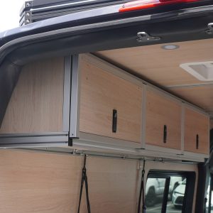 3-door birch overhead cabinet closed with compression latches viewed from rear door opening of a Mercedes Sprinter van conversion by New Way Van Life