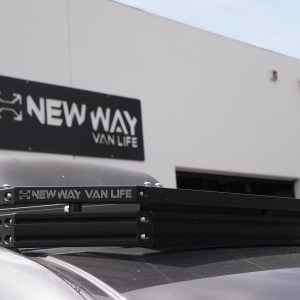 New Way Van Life branded black aluminum roof rack on a Mercedes Sprinter van with Houghton AC unit mounted on platform and New Way Van Life shop sign prominently visible in background