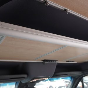 Cockpit upper shelf installed in a Mercedes Sprinter van conversion showing birch laminate surface, aluminum extrusion frame, and mounting hardware positioned above the cab area
