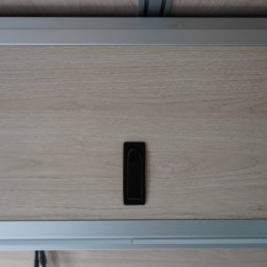Front-facing view of a birch laminate overhead cabinet door panel with centered black compression latch mounted in aluminum extrusion frame in a Mercedes Sprinter van conversion by New Way Van Life