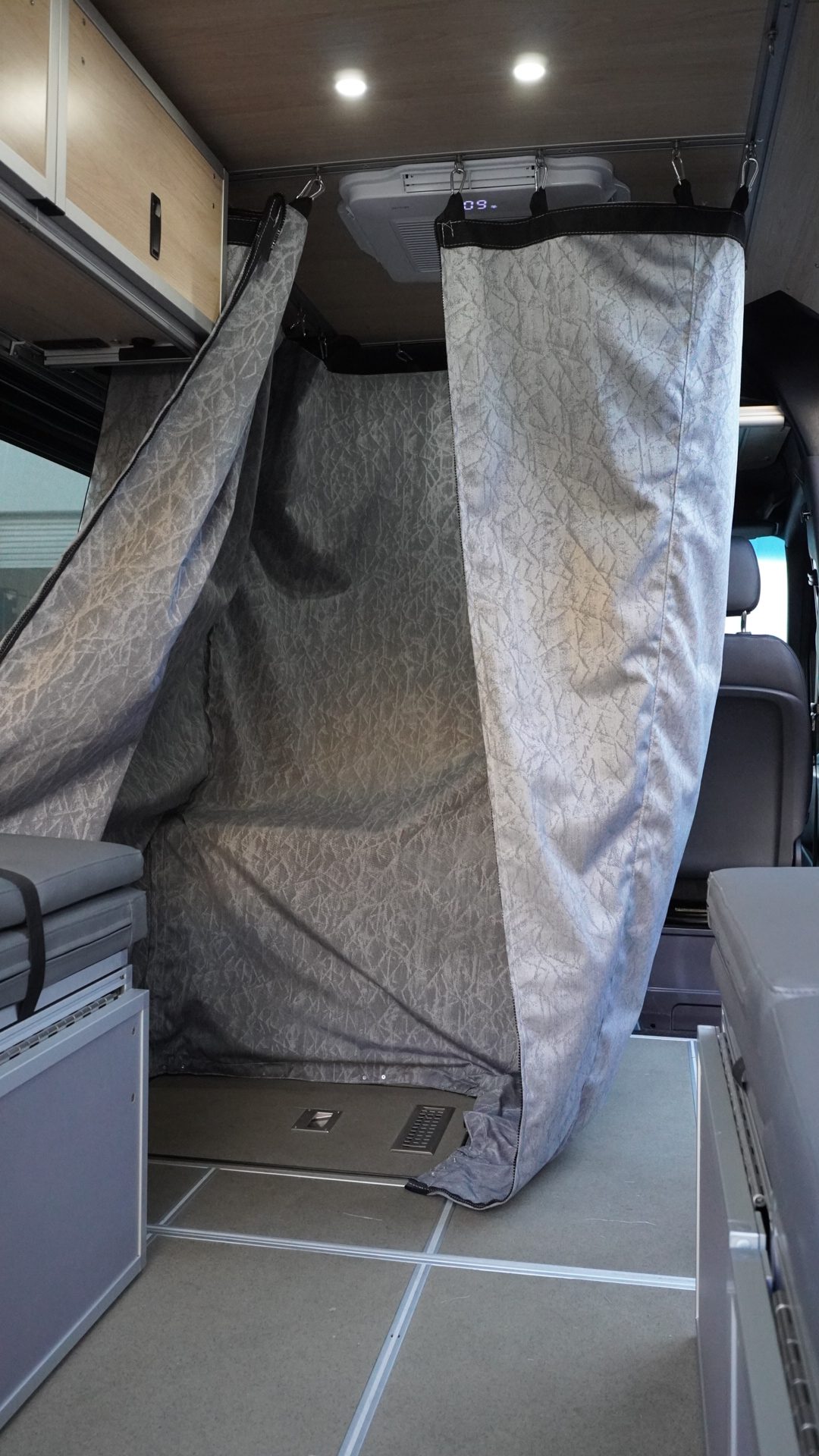 Custom Sunbrella water-resistant shower curtain fully deployed as a shower enclosure inside a Mercedes Sprinter van conversion showing the shower pan drain, ceiling mount hardware, and full interior context by New Way Van Life