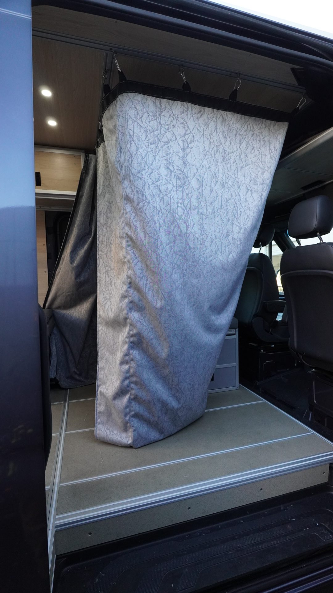 Custom Sunbrella water-resistant shower curtain hanging from ceiling track hardware in the sliding door opening of a Mercedes Sprinter van conversion by New Way Van Life