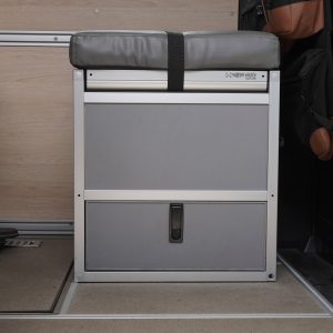 New Way Van Life Wrappon toilet cabinet with gray vinyl cushion top and retention strap closed inside a Mercedes Sprinter van conversion